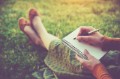 female hands with pen writing on notebook on grass outside